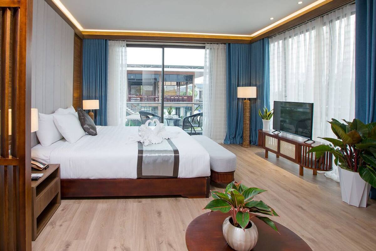 Une chambre d’hôtel moderne avec un grand lit, une télévision, une table de chevet en bois et une plante en pot.