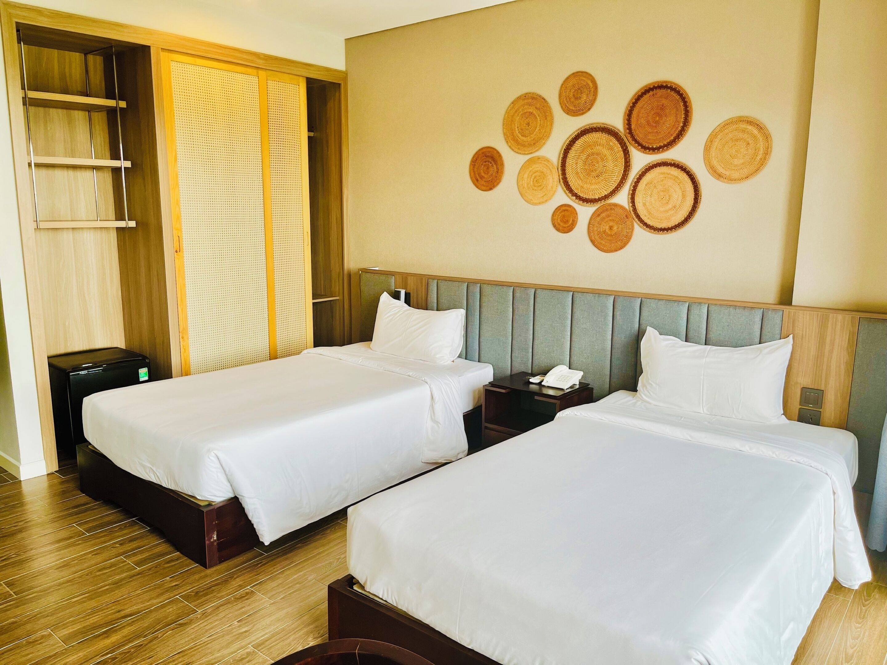 A hotel room with two beds, a wardrobe, a desk, and a wall with circular woven decorations.