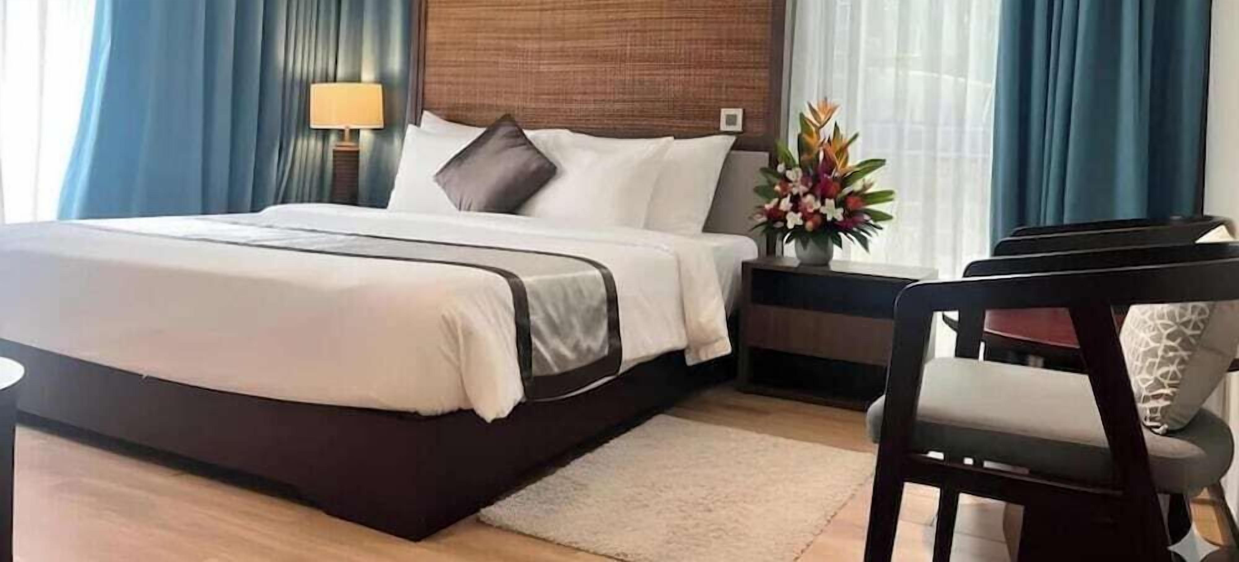 Ein Hotelzimmer mit Bett, Nachttisch, Lampe, Stuhl und einer Blumenvase.