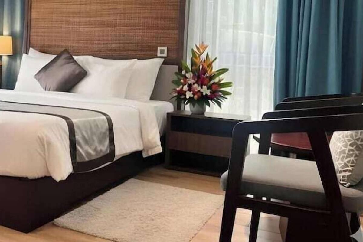 Ein Hotelzimmer mit Bett, Nachttisch, Lampe, Stuhl und einer Blumenvase.
