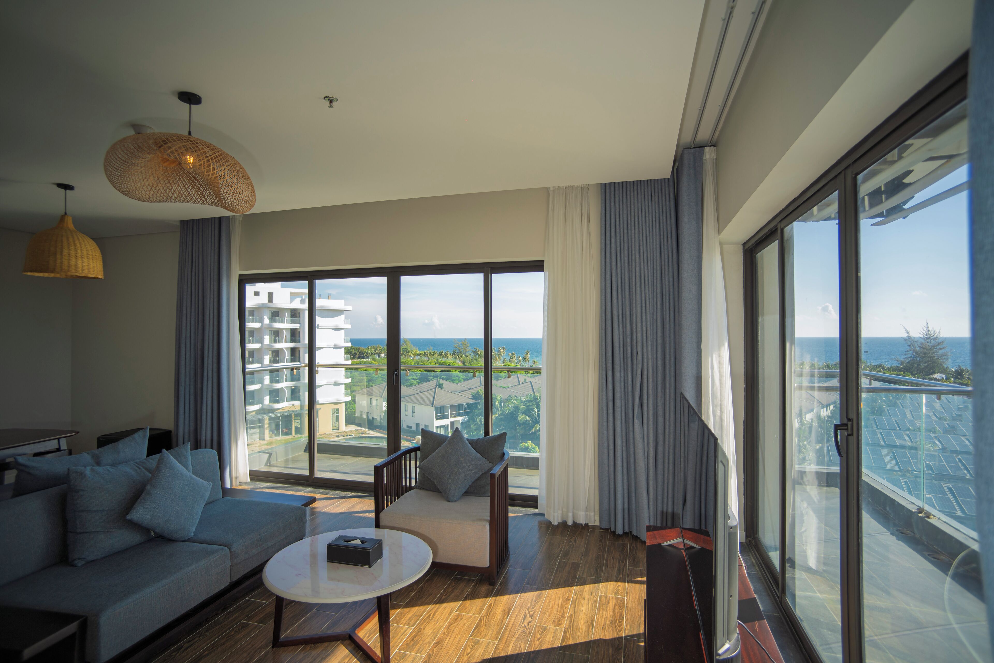 Una sala de estar moderna con un sofá, una mesita y una silla. Se ve un ventanal con vistas a edificios y una masa de agua.