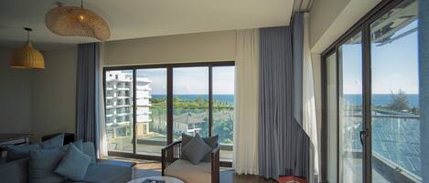 Una sala de estar moderna con un sofá, una mesita y una silla. Se ve un ventanal con vistas a edificios y una masa de agua.