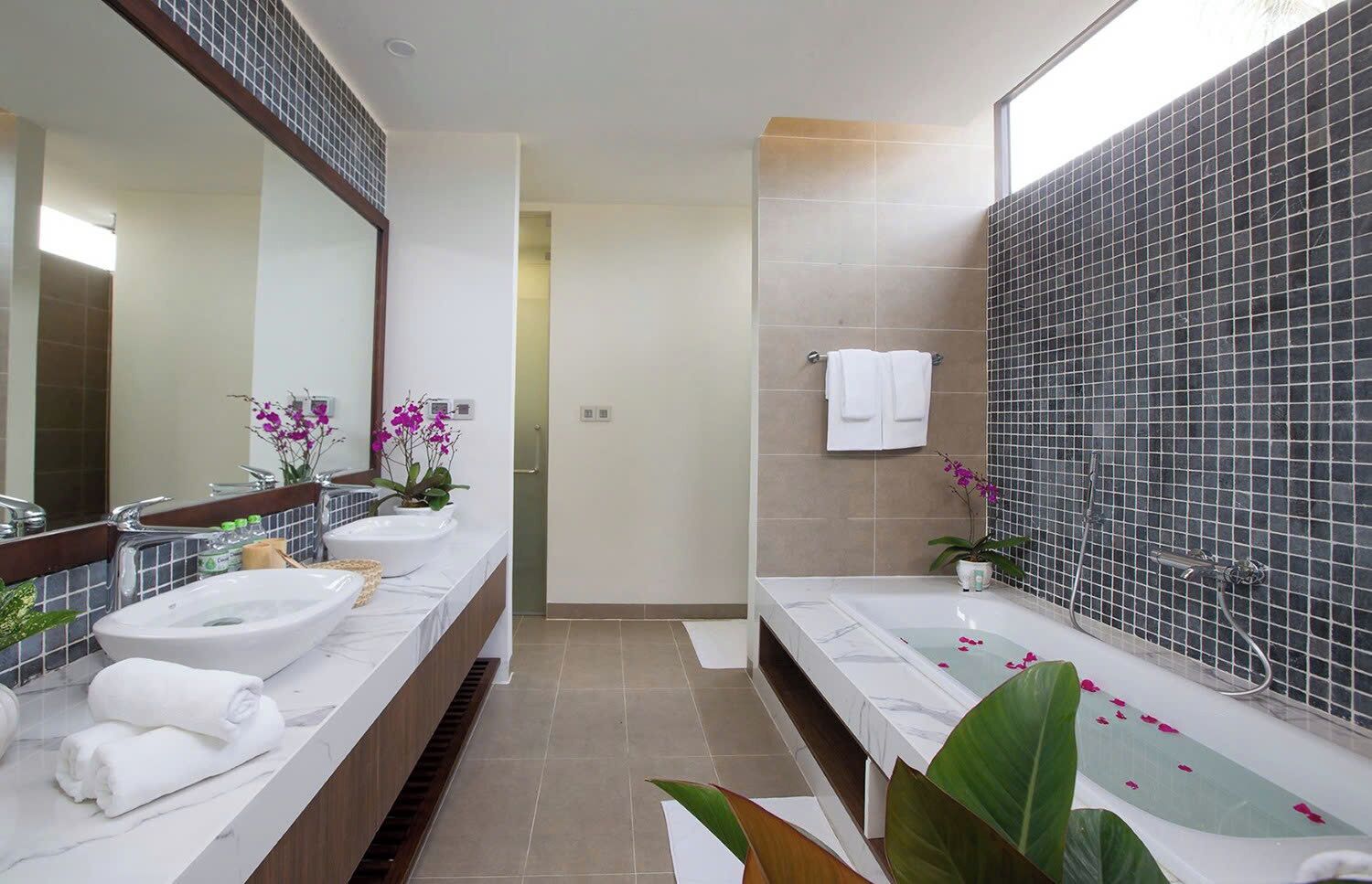 A modern bathroom with two sinks, a large mirror, and a bathtub.