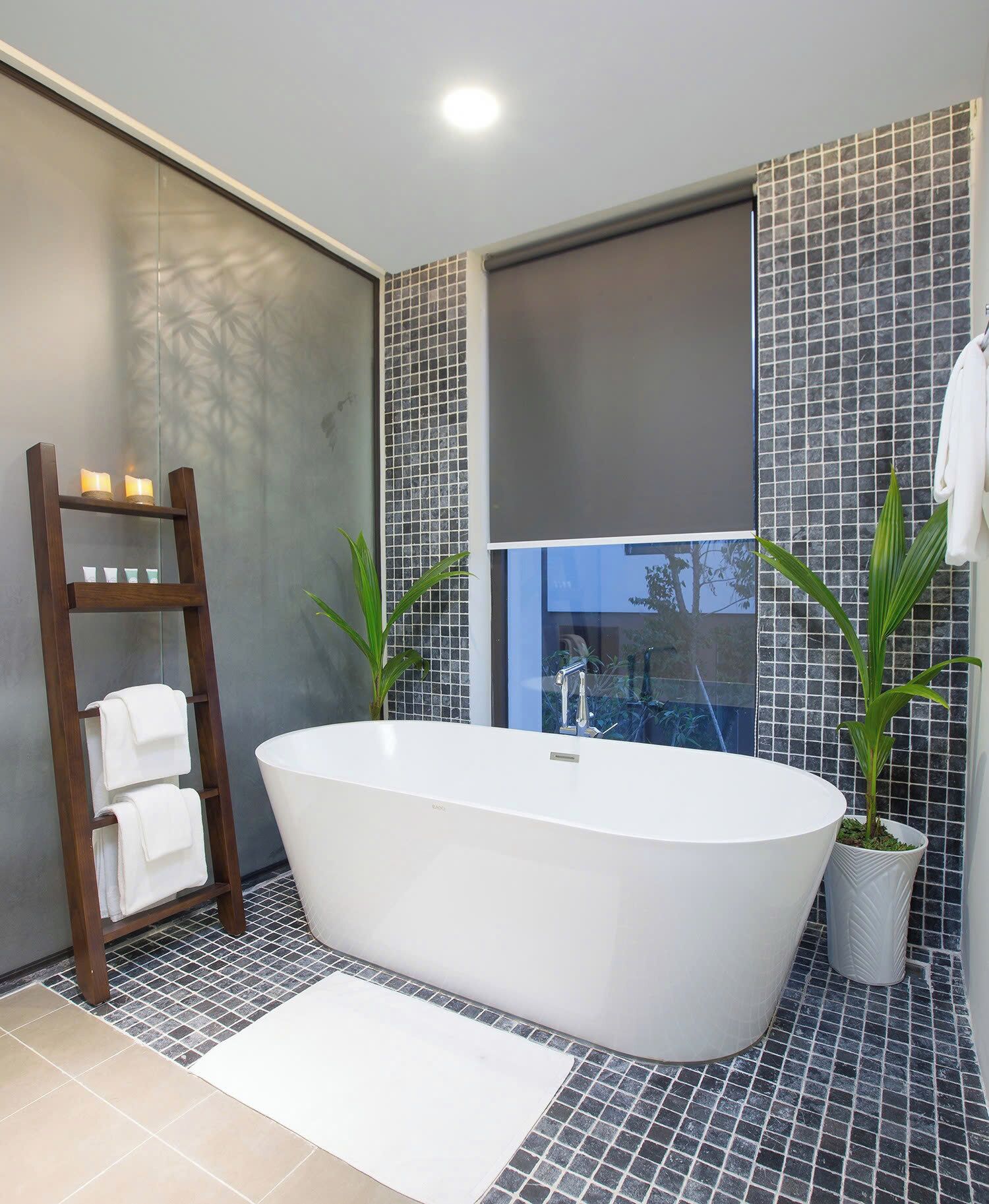 Un baño moderno con una bañera independiente, un perchero de madera y dos plantas en macetas.