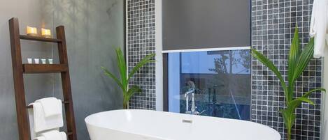 Un baño moderno con una bañera independiente, un perchero de madera y dos plantas en macetas.
