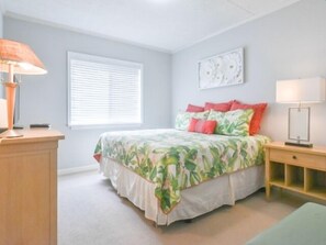 Ein Schlafzimmer mit einem Bett, einem Nachttisch, einer Lampe, einem Fenster mit Jalousien und einem Wandbild.