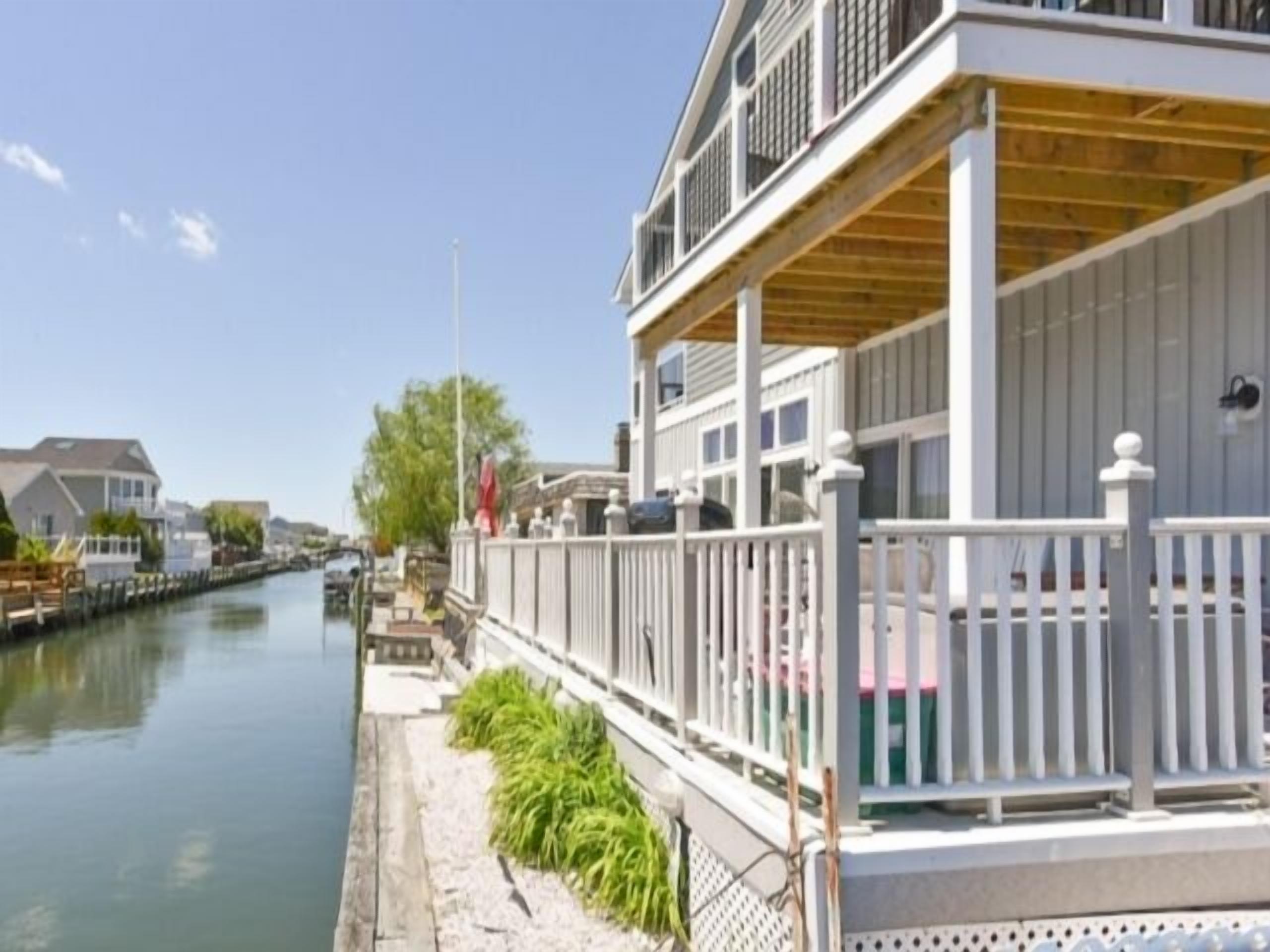 A waterfront property with a covered deck, a canal, and adjacent buildings.