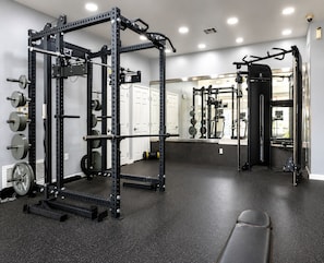 A gym with a squat rack, weight plates, and a bench. - Amber Tide - Bright 1BR Marina Gem Ocean View (Marina Del Rey)