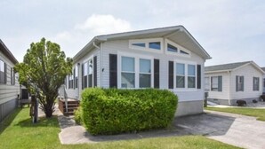 A single-story mobile home with a front porch, a small tree, and a well-maintained lawn.