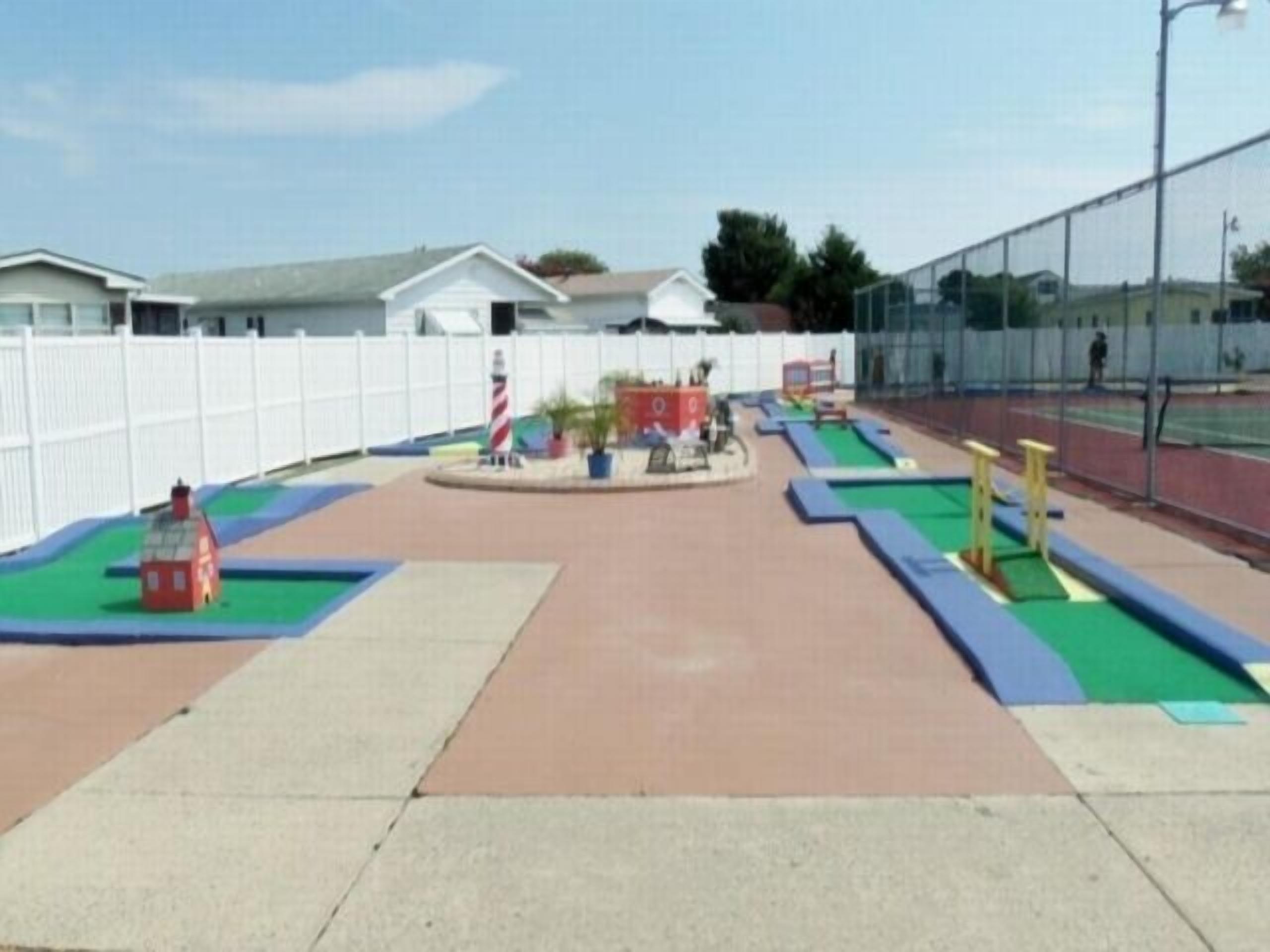 Une aire de jeux avec une zone délimitée par une clôture, un petit bâtiment rouge et un terrain de sport.