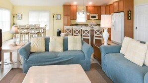 A living room with a blue sofa, a coffee table, and a dining area with a table and chairs. - Montego Bay Community Canal Front  wrap around porch, boat tie up, Pools, Tennis N. Ocean City MD! (Ocean City)