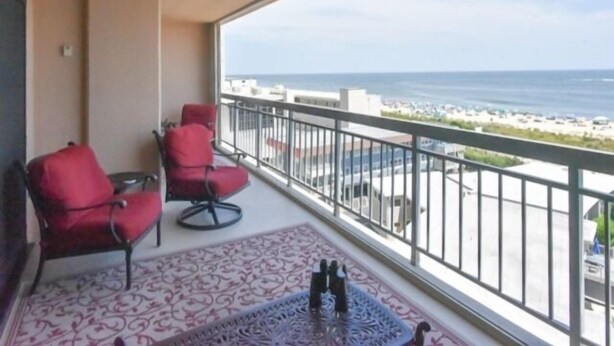Un balcon avec deux chaises rouges, un tapis à motifs et une vue sur la plage et l’océan.