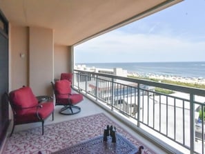 Un balcon avec deux chaises rouges, un tapis à motifs et une vue sur la plage et l’océan.