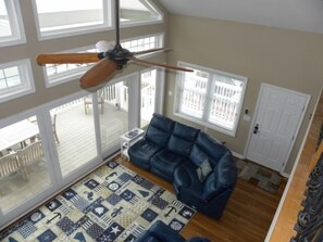 A spacious living room with a blue leather sofa, a patterned rug, and a ceiling fan. - Direct Bay Front,  Panoramic Bay and Sunset Views, Boat Dock/Slip, Large porch on the wide open bay! (Ocean City)