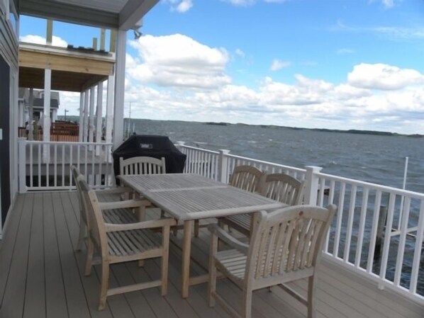 A wooden deck with a table and chairs, a grill, and a white railing overlooking a body of water.