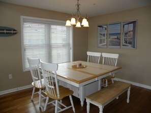 A dining area with a wooden table, white chairs, and a bench. There are three pendant lights above the table. - Direct Bay Front,  Panoramic Bay and Sunset Views, Boat Dock/Slip, Large porch on the wide open bay! (Ocean City)