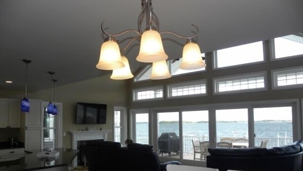 A spacious kitchen with a large island, a dining area with white chairs, and a view of the water through large windows. - Direct Bay Front,  Panoramic Bay and Sunset Views, Boat Dock/Slip, Large porch on the wide open bay! (Ocean City)