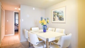 Ein Essbereich mit weißem Tisch und Stühlen, einer Vase mit Blumen und einem Gemälde an der Wand.