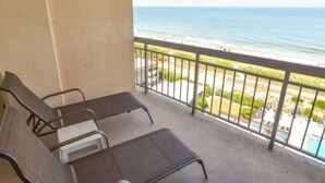 Ein Balkon mit zwei Liegestühlen und einem kleinen Tisch, mit Blick auf einen Strand und das Meer.