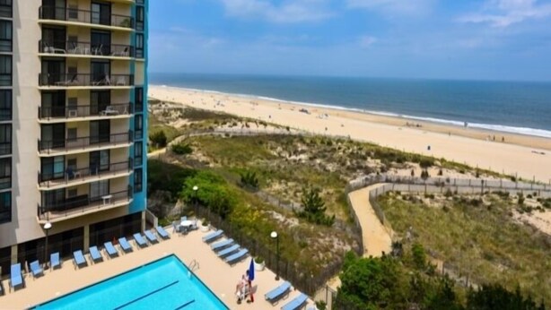 A hotel with a pool, a beach view, and a building with multiple balconies. - Ocean Front Building w/ side views of Ocean and Beach, lifeguarded pool, Game Room, Gym, Tennis (Ocean City)