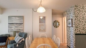 A dining area with a wooden table and white chairs, a hanging light fixture, and a wall with a floral pattern. - Ocean Front Building w/ side views of Ocean and Beach, lifeguarded pool, Game Room, Gym, Tennis (Ocean City)