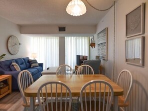 Uma sala de jantar com mesa de madeira e cadeiras brancas, um sofá azul e um relógio na parede.