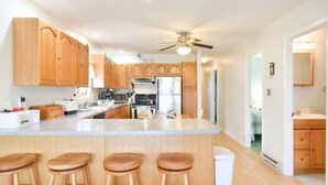 A modern kitchen with wooden cabinets, a central island with stools, a ceiling fan, and a view into the adjacent living area. - Montego Bay Community BAY VIEW 4 BR 2 Bath w/ screened porch! 2 large community pools & tennis (Ocean City)