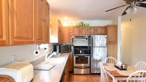 A compact kitchen with wooden cabinets, a stainless steel refrigerator, a microwave, and a dining area with a wooden table and white chairs. - Montego Bay Community BAY VIEW 4 BR 2 Bath w/ screened porch! 2 large community pools & tennis (Ocean City)