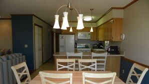 Un espace repas avec une table et des chaises, une cuisine en arrière-plan et des luminaires suspendus au-dessus.
