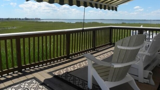 Un balcon donnant sur un plan d’eau, un auvent à rayures et deux fauteuils Adirondack.