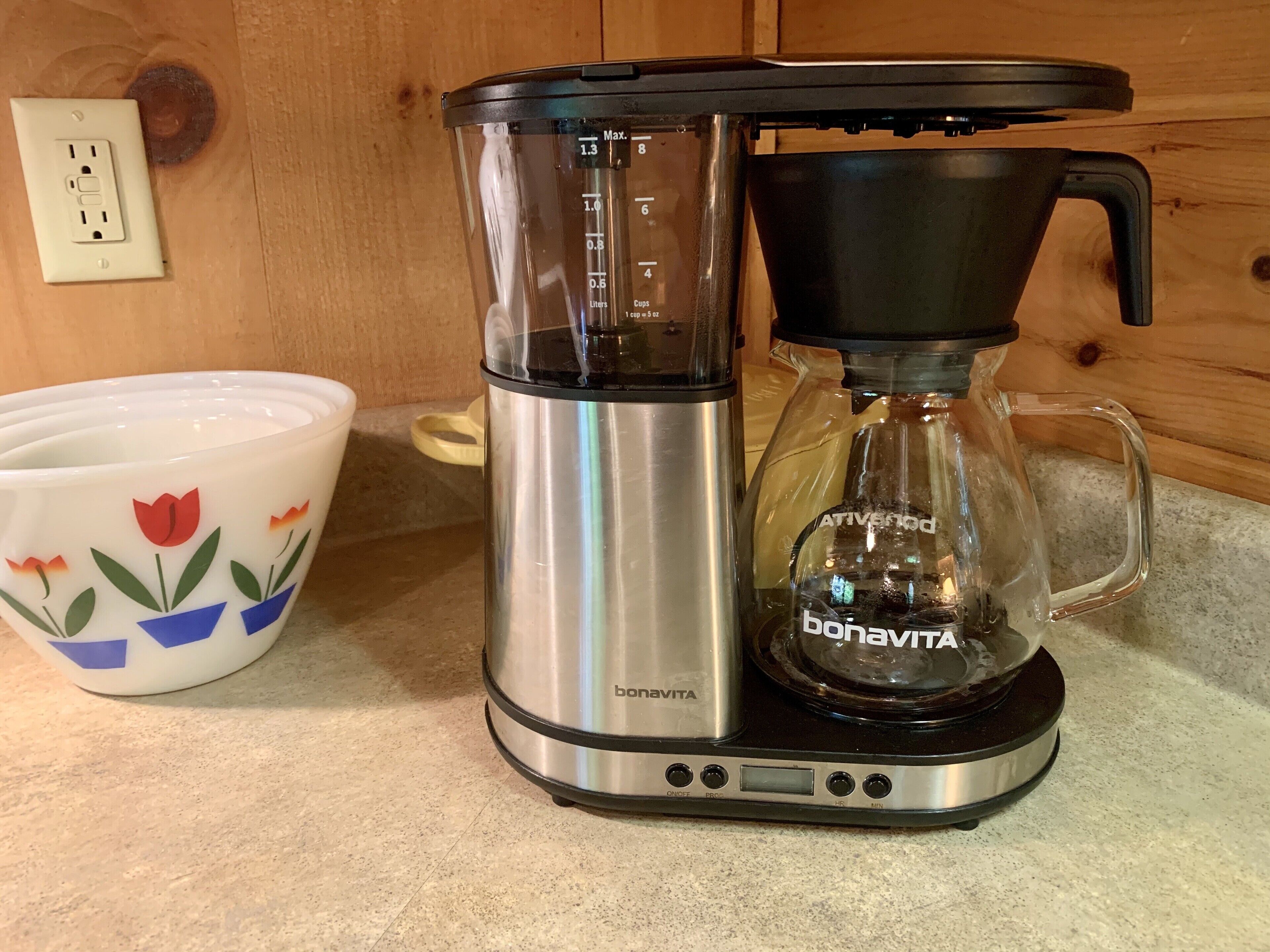 Uma cafeteira com visor digital e jarra de vidro em uma bancada de cozinha.
