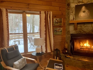 A cozy cabin interior with a fireplace, a comfortable chair, a table with a lamp, and framed pictures on the wall. - Cozy Mountain Cabin in Aska Wilderness with Saltwater Hot Tub in Blue Ridge, GA (Blue Ridge)