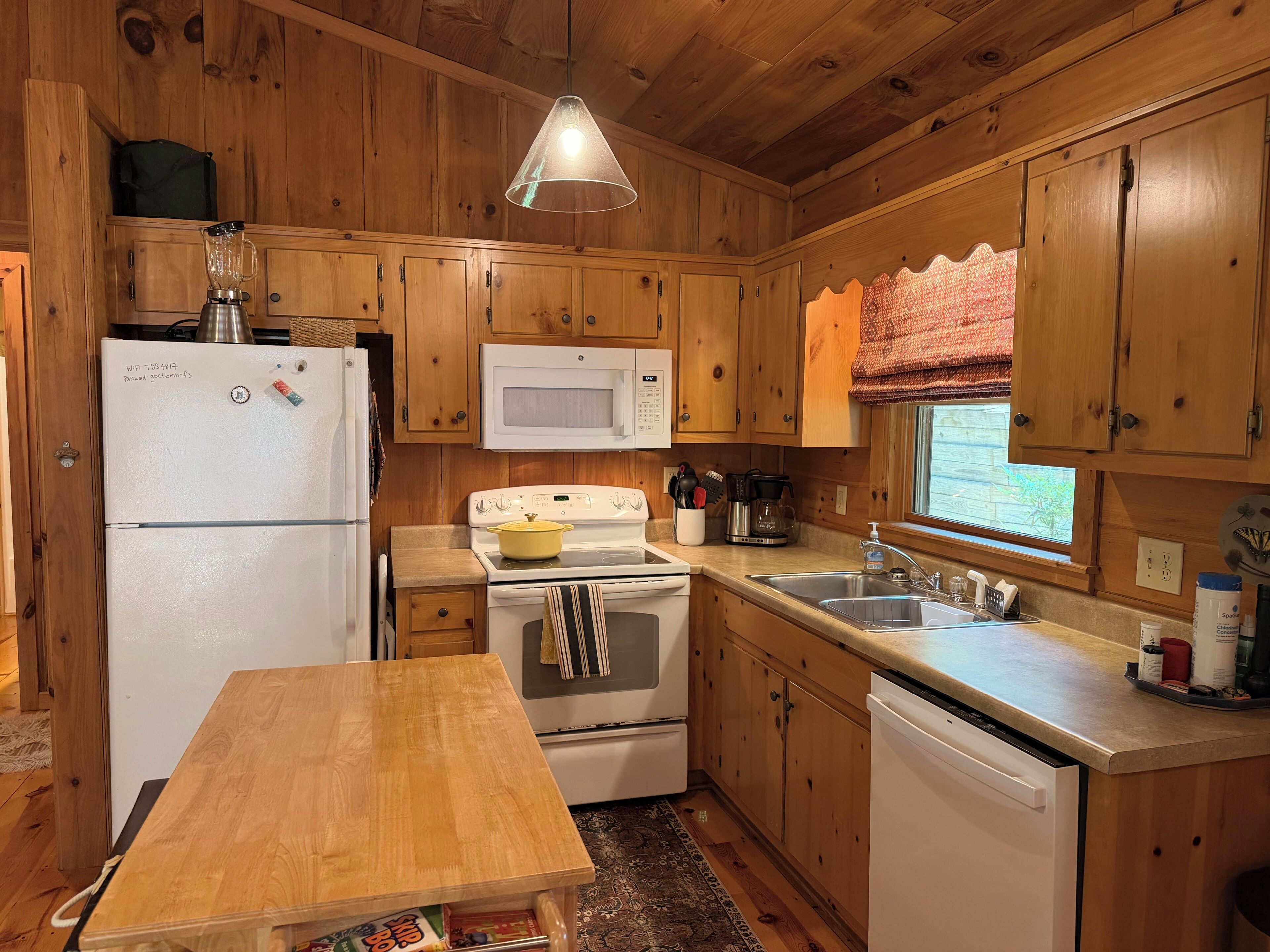 Une cuisine avec des meubles de rangement en bois, un réfrigérateur, un four à micro-ondes, un four, un évier et une table en bois.