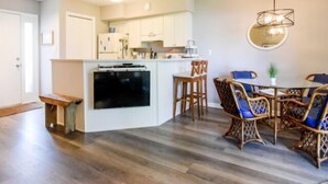Una cocina moderna con armarios blancos, horno integrado y un comedor con sillas de mimbre y mesa de vidrio.