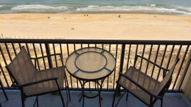 Ein Balkon mit Glastisch und zwei Stühlen mit Blick auf einen Strand und das Meer.