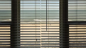 Blick durch Jalousien auf einen Strand mit Wellen und Sand.