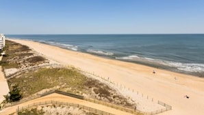 Ein Strand mit sandigem Ufer, einigen Personen und einem Gebäude im Hintergrund.