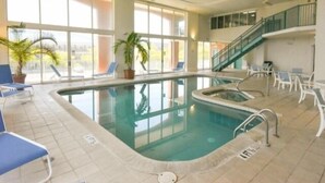 An indoor swimming pool with clear glass walls, blue lounge chairs, and a staircase leading to an upper level. - Ocean Block,  porch, jacuzzi tub, indoor pool, sauna, gym! Steps from the beach! (Ocean City)