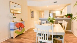 A dining area with a white table and chairs, a small side table with a plant, and a decorative item on the wall. - Ocean Block,  porch, jacuzzi tub, indoor pool, sauna, gym! Steps from the beach! (Ocean City)