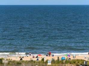 A beach with people, umbrellas, and a fence. - Ocean Block,  porch, jacuzzi tub, indoor pool, sauna, gym! Steps from the beach! (Ocean City)