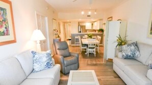 A living room with two sofas, a coffee table, and a ceiling fan. There is a dining area with a table and chairs in the background. - Ocean Block,  porch, jacuzzi tub, indoor pool, sauna, gym! Steps from the beach! (Ocean City)