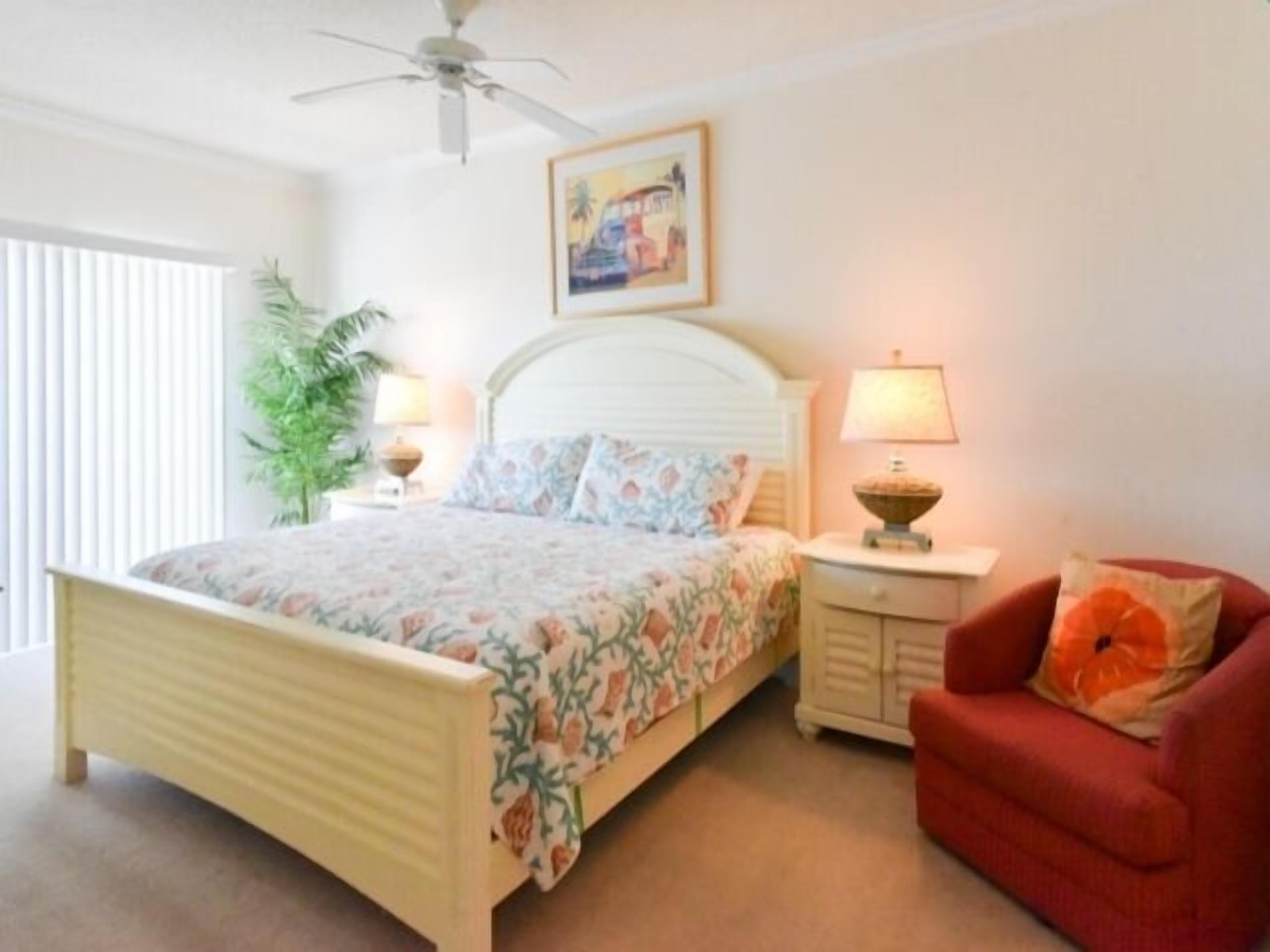 A bedroom with a bed, a nightstand, a chair, a ceiling fan, and a wall-mounted painting.