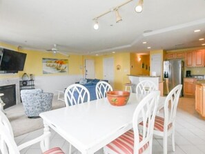 A bright living room with a white table and chairs, a sofa, and a TV mounted on the wall.