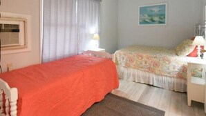 A bedroom with two beds, a window with curtains, a bedside table with a lamp, and a painting on the wall. - Ocean Block Condo, Steps from the beach, full kitchen, W/D, 1 Parking Spot , North Ocean City! (Ocean City)