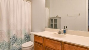 A bathroom with a toilet, wooden cabinets, a sink, and a mirror. - Ocean Block Condo, Steps from the beach, full kitchen, W/D, 1 Parking Spot , North Ocean City! (Ocean City)