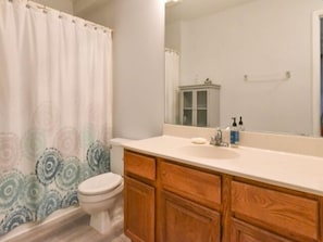 A bathroom with a toilet, wooden cabinets, a sink, and a mirror.