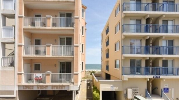 A multi-story residential building with balconies, a parking area, and a view of the beach. - Ocean Block Condo, Steps from the beach, full kitchen, W/D, 1 Parking Spot , North Ocean City! (Ocean City)
