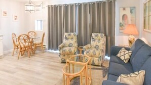 A living room with a blue sofa, patterned armchairs, a dining table with chairs, and a ceiling fan. - Ocean Block Condo, Steps from the beach, full kitchen, W/D, 1 Parking Spot , North Ocean City! (Ocean City)