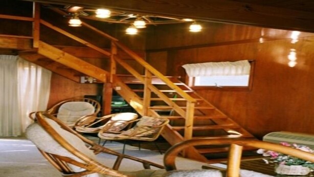 Un interno in legno con una scala, mobili in vimini e una finestra con tende.