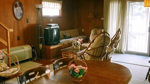 Un accogliente soggiorno con un tavolo in legno, sedie, una televisione e una finestra con tende.